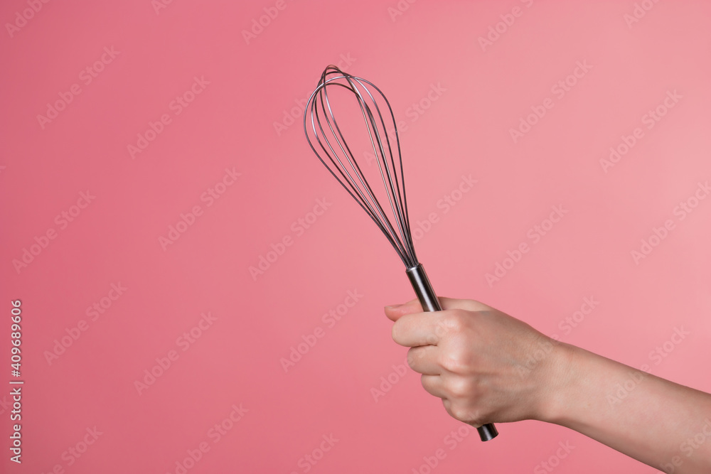 Whisk for whipping cream, making desserts. A woman's hand and kitchen tools. pastry chef on a pink background. copy space Whisk for whipping cream, making desserts. A woman's hand and kitchen tools. pastry chef on a pink background. copy space