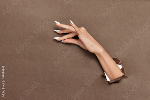 Valokuva Female hand with long white nails sticking out of brown paper background