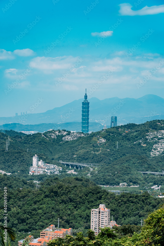 View of Taipei 101 tower with green forests and mountains in the foreground.