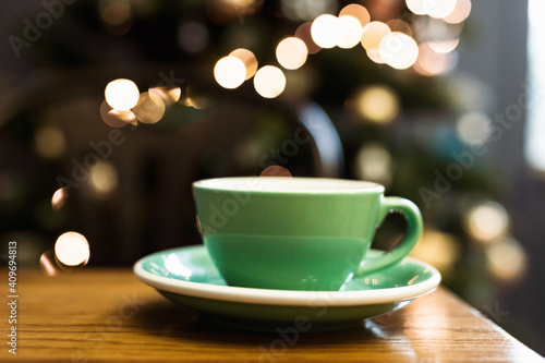 A horizontal lifestyle photo of a green cup of black coffee on a saucer, a spoon, bokeh lights in the background, selective focus