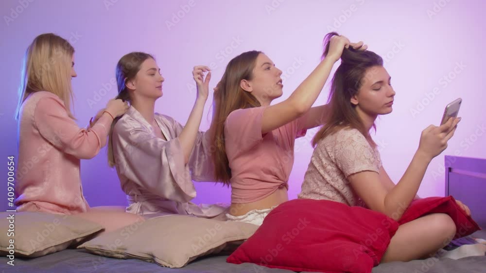 Four happy pretty young women in pajamas sits on bed and ties pigtails to each other at bachelorette party Four happy pretty young women in pajamas sits on bed and ties pigtails to each other at bachelorette party