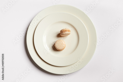 Two light macaroons in a light plate on a light background, minimalist composition, top view