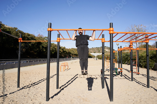Young man doing pull up, calisthenics. Outdoor barbell exercise, fitness, sport, training and lifestyle concept.
