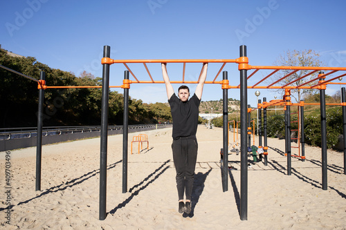 Young man in a barbell park doing pull up, calisthenics. Outdoor barbell exercise, fitness, sport, training and lifestyle concept.