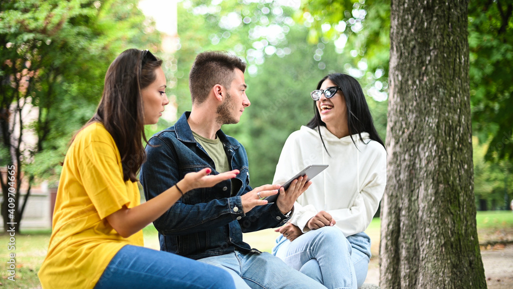 Three students studying together with a digital tablet sitting on a bench outdoor Three students studying together with a digital tablet sitting on a bench outdoor