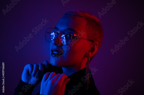 Close-up portrait of young blonde woman with short hair wearing glasses in neon light