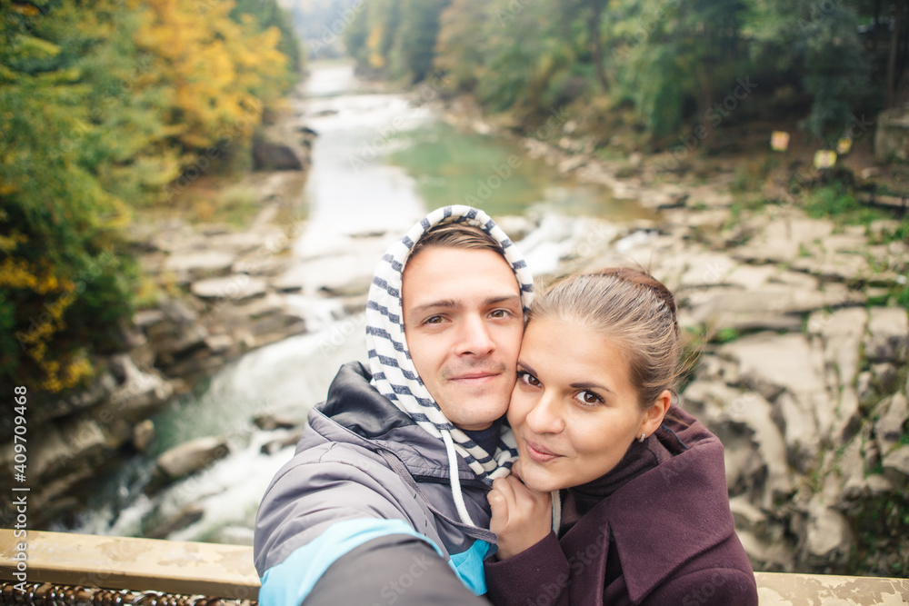 young beautiful couple travelers take a photo on the background of the river and forest