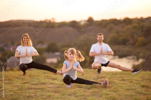 Happy healthy active family of three do gymnastic exercises together outdoor at sunset. Focus on little girl