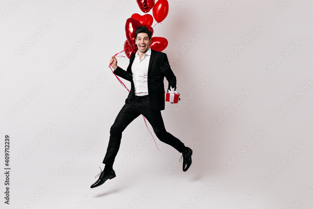 Full length shot of handsome man jumping with air balloons. Caucasian guy posing in valentine's day isolated on white.