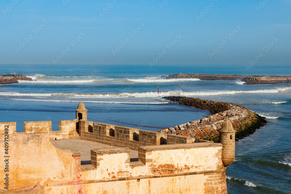 The medieval bastion of Kasbah of the Udayas with two small turrets and the breakwaters that separate the Bou Regreg river mouth from the Atlantic Ocean on a sunny morning. Rabat, Morocco.