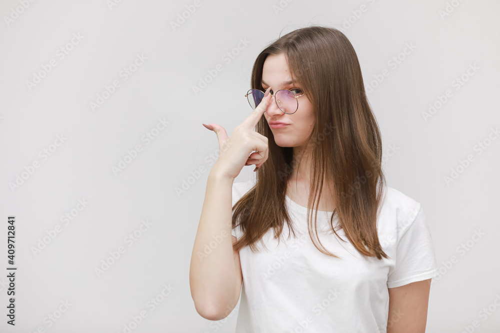 Focused frowning office girl staring at camera through eyeglasses on white background. Young woman adjusting eyewear. Glasses wearing concept Focused frowning office girl staring at camera through eyeglasses on white background. Young woman adjusting eyewear. Glasses wearing concept