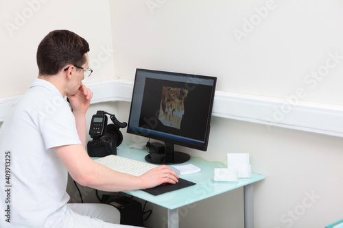 Dentist doctor examines images of teeth on a computer screen. Modern dentistry. Volumetric image. Photo camera on the desktop. Photo in the interior.