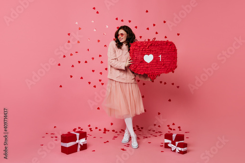 Full length shot of girl with valentine gifts. Studio photo of lady in pink skirt hlding heart symbol. photo