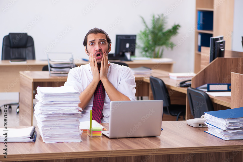 Young male employee unhappy with excessive work in the office Young male employee unhappy with excessive work in the office