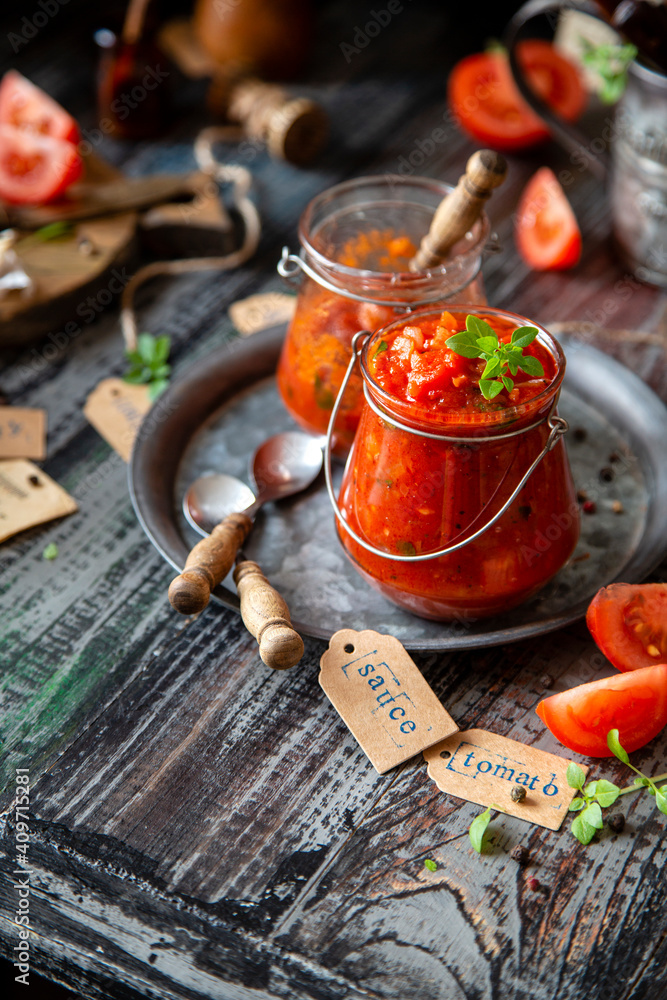 homemade red tomato sauce in glass jar on metal plate on wooden table with basil leaves