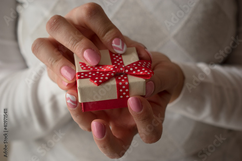 Woman hands holding a small present box with red ribbon over. Valentine gift box.