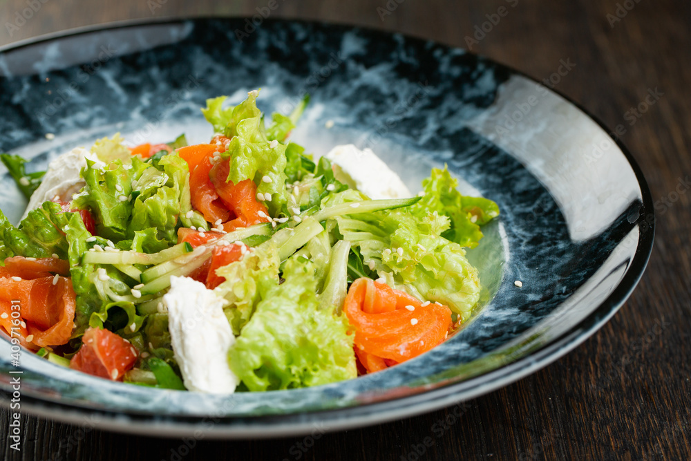 Greek salad of tomatoes, pickled peppers, cucumbers, lettuce and feta cheese. greek salad with olives and white sesame seeds on a blue marble plate Greek salad of tomatoes, pickled peppers, cucumbers, lettuce and feta cheese. greek salad with olives and white sesame seeds on a blue marble plate