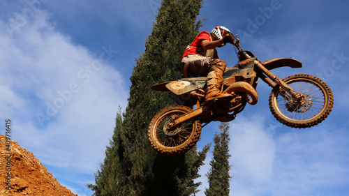 Professional dirt bike motocross rider performing stunts and flying from jump in extreme terrain track