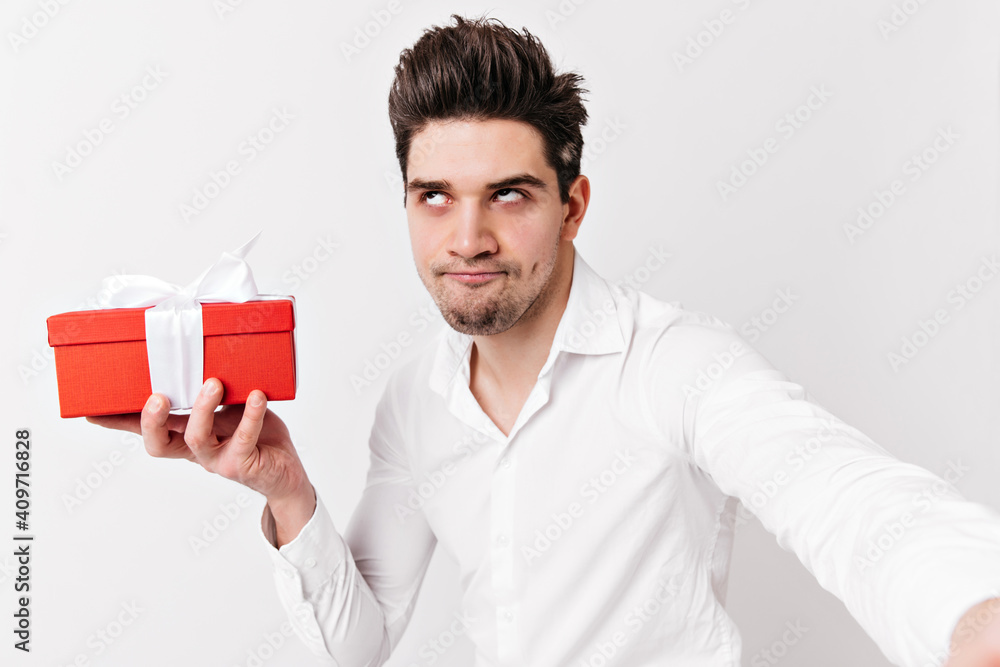 Funny caucasian man in shirt holding present. Studio shot of emotional brunette guy celebrating valentine's day. Funny caucasian man in shirt holding present. Studio shot of emotional brunette guy celebrating valentine's day.