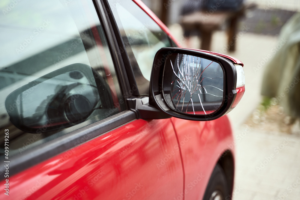 Red car with broken side door mirror parked on the street
