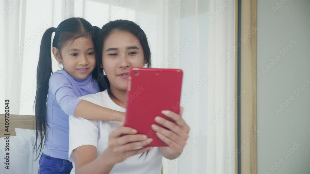 Young asian mom and daughter video call on tablet computer greeting with family together, happy mother and girl with relationship using technology in communication to internet online, two people. Young asian mom and daughter video call on tablet computer greeting with family together, happy mother and girl with relationship using technology in communication to internet online, two people.
