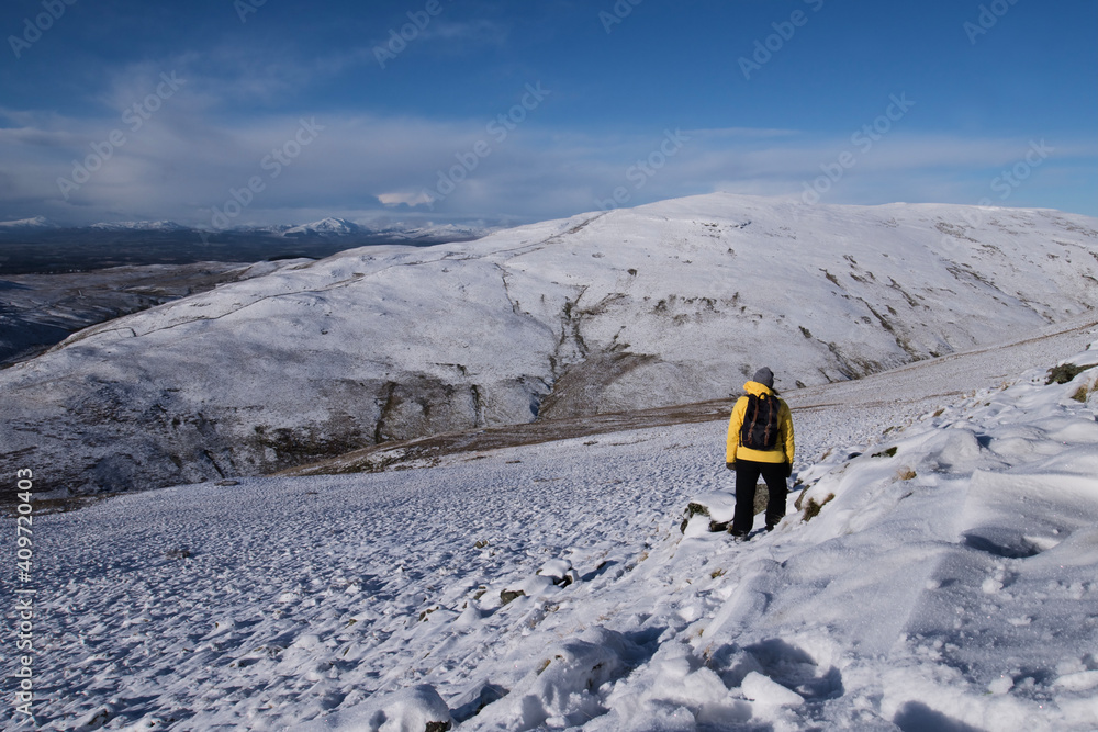girl in winter gear hiking in snow covered hills in Scotland on a bright blue day