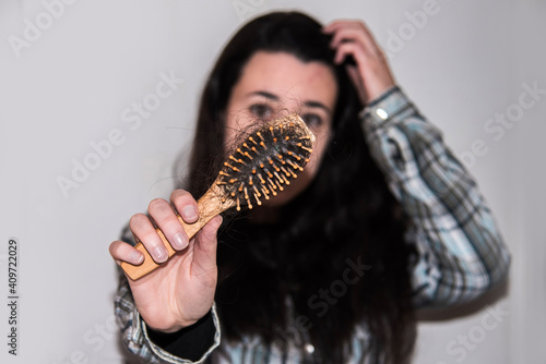 Mujer joven sujetando con la mano un cepillo con pelo caído mientras mira directamente a la cámara. Concepto de caída del cabello photo