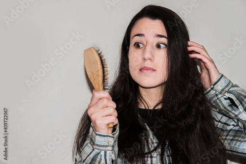 Mujer joven sujetando con la mano un cepillo con pelo caído mientras tiene una expresión de shock y sorpresa. Concepto de caída del cabello