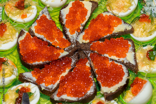 Black bread with caviar on a tray around stuffed chicken eggs. Canapes with red caviar on rye bread.