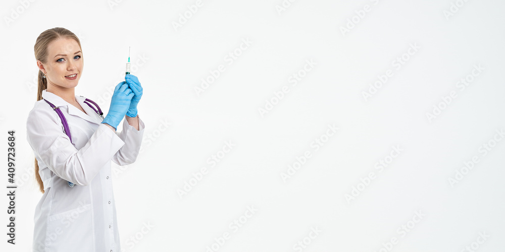 A young nurse in a mask and white coat holds a syringe with a needle for injections, flu shots, covid. The concept of vaccination and protection against influenza, from a pandemic. copy space. banner A young nurse in a mask and white coat holds a syringe with a needle for injections, flu shots, covid. The concept of vaccination and protection against influenza, from a pandemic. copy space. banner