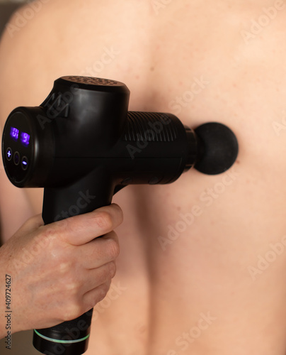 Therapist treating Injury of man . Massage Gun, used by professionals to massage the body. Sport physical therapy concept.