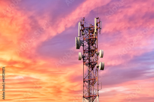 Telecommunication tower with antennas against beautiful colorful sky at sunset or dawn with pink clouds background.