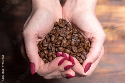 Fresh roasted coffee beans pouring out of cupped woman hands on a wooden background
