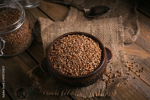 Organic uncooked scattered buckwheat grain in a bowl and glass jar on a rustic wooden background