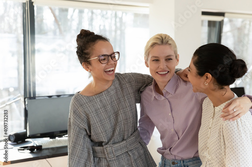 Excited female multiethnic team of office employees celebrating corporate win, work success, job promotion. Happy mixed raced intern girls embracing together. Business achievement concept