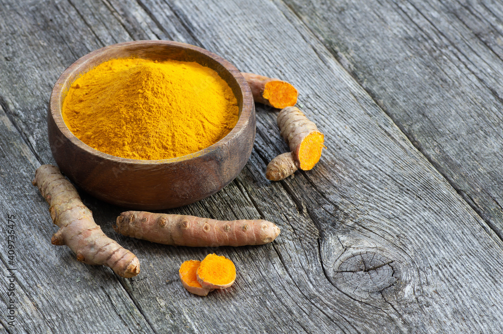 Turmeric powder in spoon or bowl and fresh turmeric root on wooden background, spice concept, ( curcuma longa )