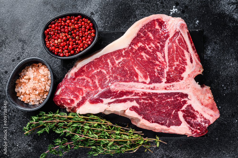 Dry-aged Raw T-bone or porterhouse beef meat Steak with herbs and salt. Black background. Top view