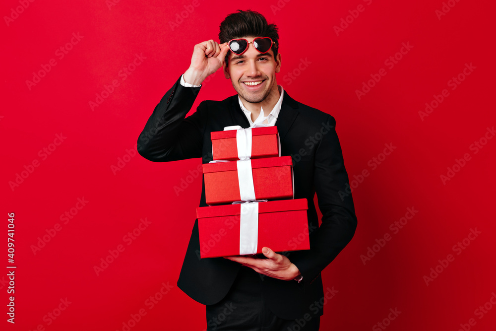 Handsome man wishing happy valentine. Studio shot of guy with presents wears heart shaped glasses. Handsome man wishing happy valentine. Studio shot of guy with presents wears heart shaped glasses.