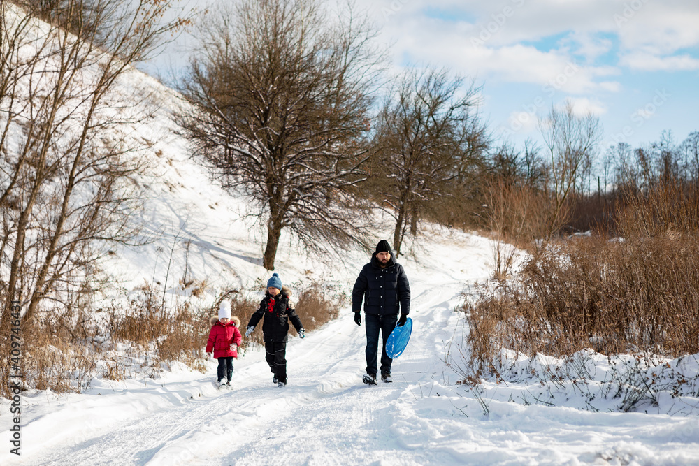 couple walking in snow. Family with child playing in the snow together in winter.Father with children go for a ride on a slide with a winter plate 