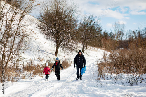 couple walking in snow. Family with child playing in the snow together in winter.Father with children go for a ride on a slide with a winter plate 