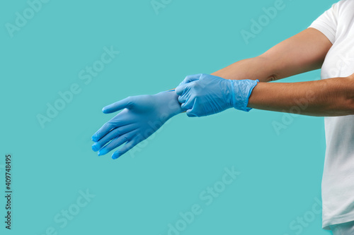 Side portrait of unrecognizable person putting on blue medical protective sterile gloves isolated on a blue background