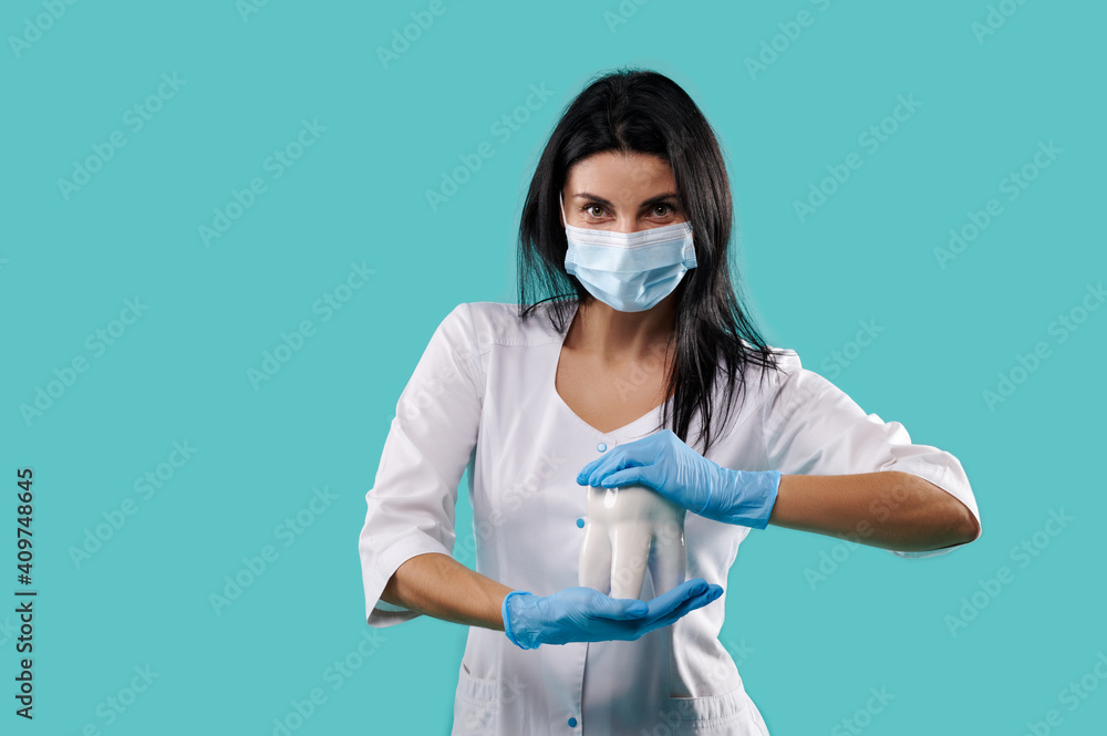 Woman dentist holding a tooth model in the hands on a blue background . Concept of healthy oral cavity. Dentistry Woman dentist holding a tooth model in the hands on a blue background . Concept of healthy oral cavity. Dentistry