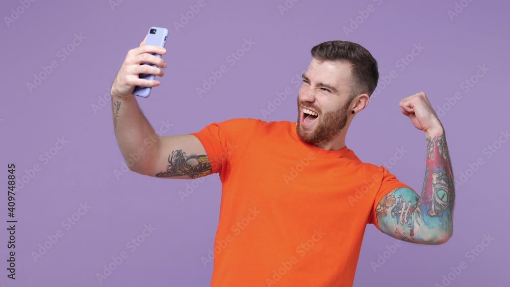 Cheerful tattooed young man isolated on violet background. People lifestyle concept. Tattoo translate life is fight. Doing selfie shot on mobile phone showing thumb up biceps muscles pointing finger Cheerful tattooed young man isolated on violet background. People lifestyle concept. Tattoo translate life is fight. Doing selfie shot on mobile phone showing thumb up biceps muscles pointing finger