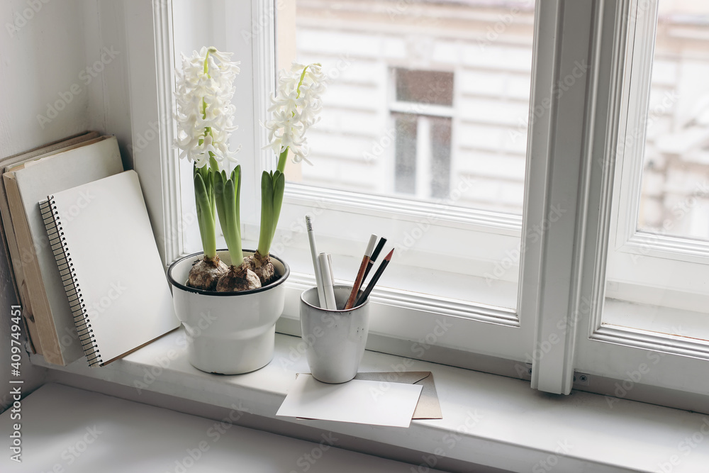 Easter spring still life. Greeting card, books and diary on window sill. White hyacinth in flower pot. Blank greeting card mockup. Pencils in ceramic holder. Home office concept. Scandinavian interior - obrazy, fototapety, plakaty 
