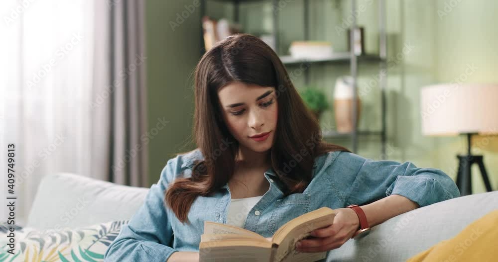 Young beautiful caucasian girl spends free time at home sitting on couch and reading interesting book. Concept of self-education. Young beautiful caucasian girl spends free time at home sitting on couch and reading interesting book. Concept of self-education.