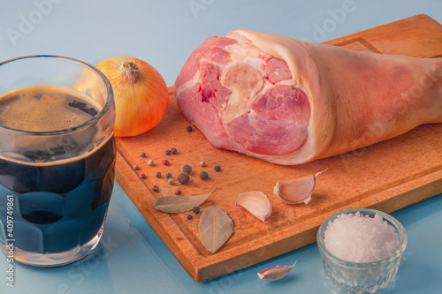 Raw pork knuckle, garlic, onion, dried bay leaves, sea salt and peppercorns on wooden cutting board.