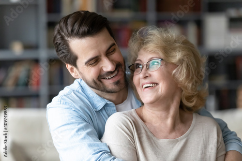Head shot close up happy young caucasian man embracing from back sincere smiling senior old retired mother, showing love care gratitude at home, different generations family relations concept.