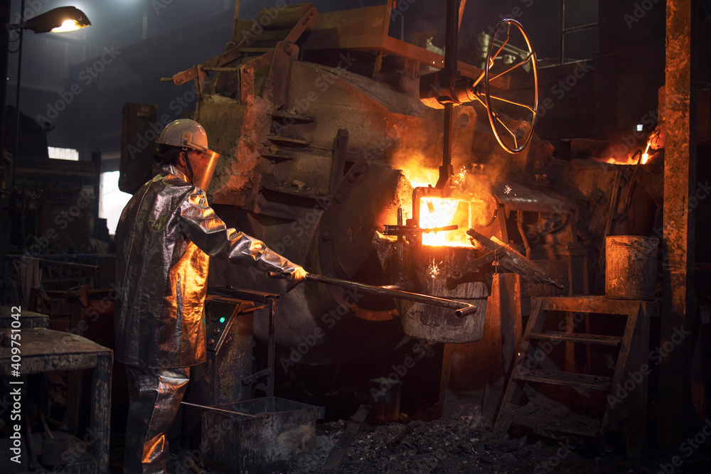 Hardworking in foundry. Workman in temperature protection suit pouring liquid metal into the bucket. Steel production.