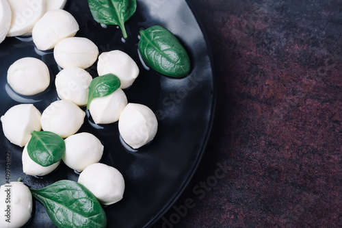 White small mozzarella cheese balls  spinach leaves and tomatoes on black plate. Top view.