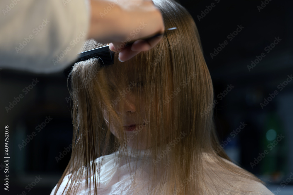 Fototapeta premium hair cutting at home, mom cuts daughter's hair in the kitchen